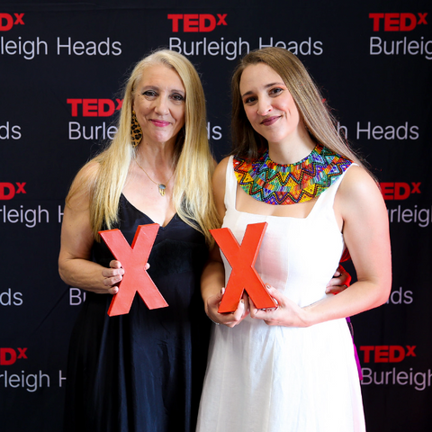 Relmi and Silvia Damiano holding red 'X' signs in front of a TEDx Burleigh Heads backdrop